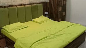 A bedroom with a bed, a green headboard, a wall-mounted light, and a ceiling fan. - Hotel SR Siddhivinayak  (Mathura)