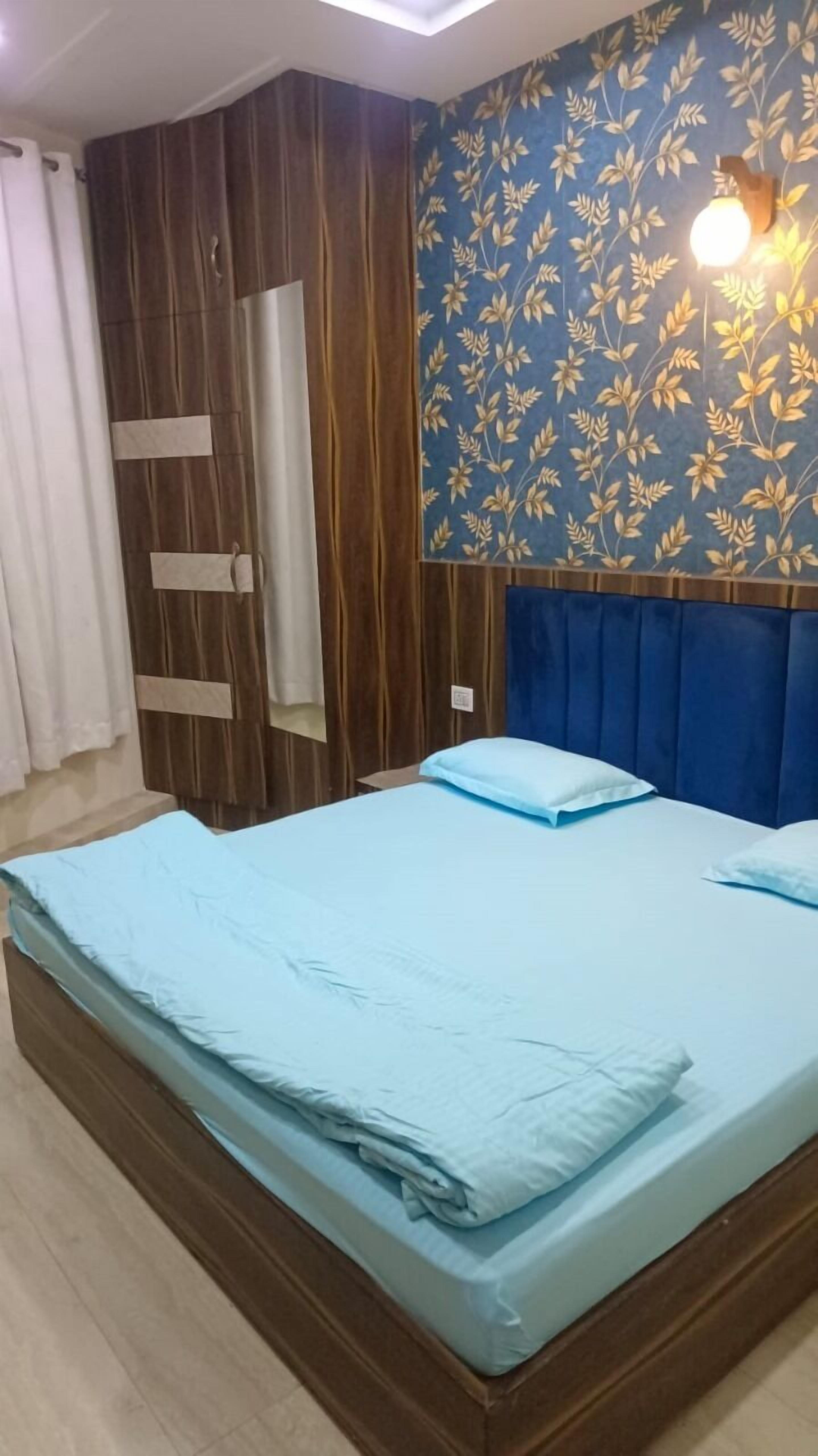 Egy hálószoba, melynek van egy fafejű ágya, egy kék, virágmintás falfelülete, és az ágyon világoskék ágynemű van.