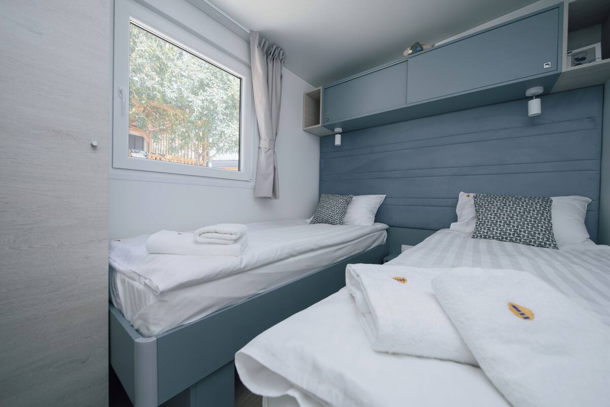 Un dormitorio con dos camas, una ventana con cortinas y una estantería empotrada sobre las camas.