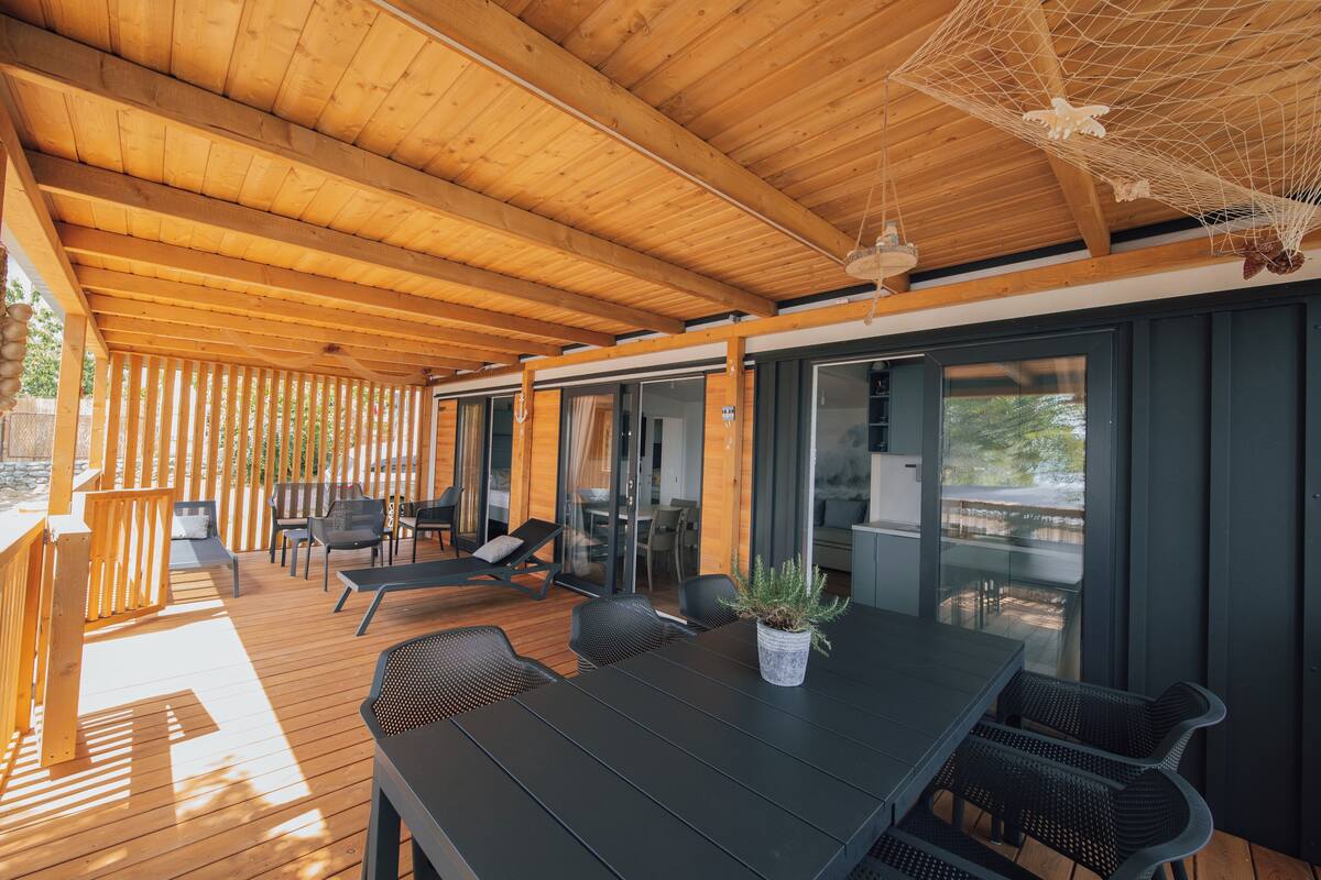 Un espacio al aire libre cubierto con suelo de madera, una mesa con sillas y una planta en maceta.
