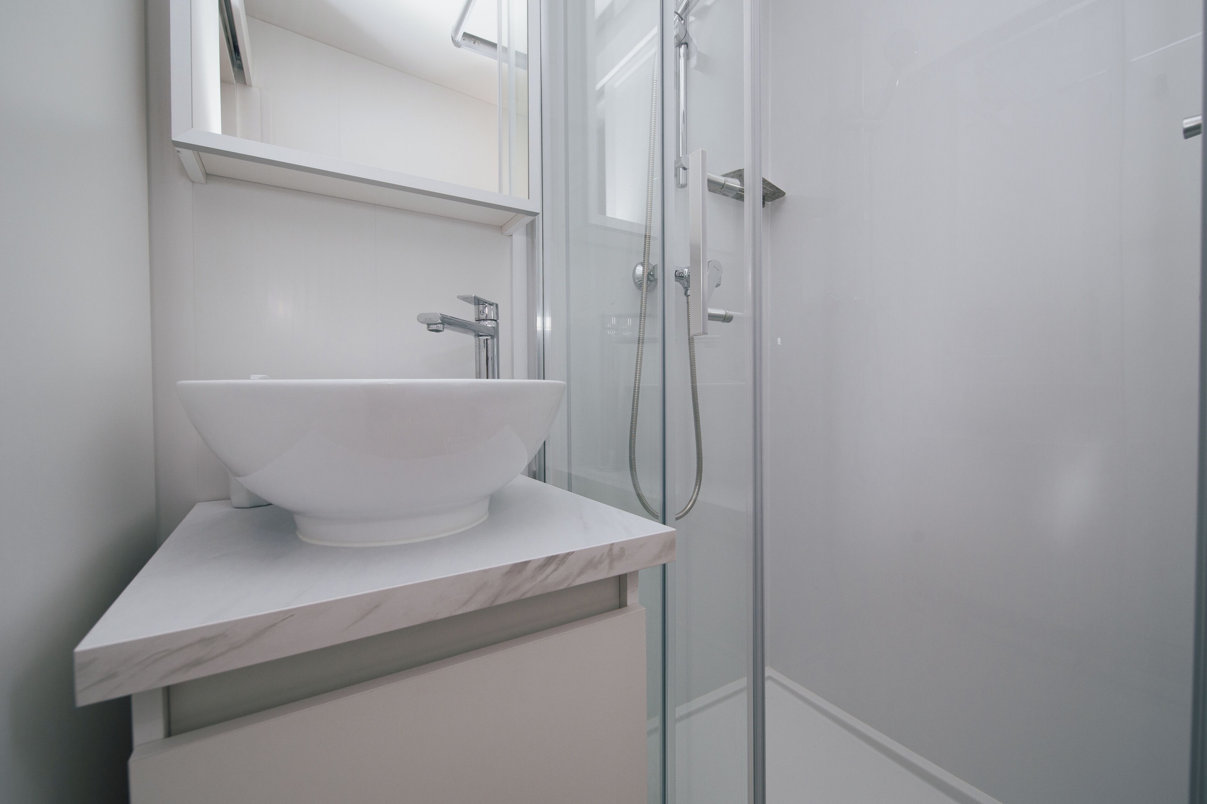 A modern bathroom with a white marble sink, a glass shower enclosure, and a large mirror above the sink.