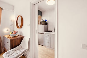 Een knus leefruimte met een kitchenette, een houten kast, een fauteuil en een spiegel.