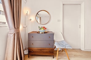 Een kamer met een houten dressoir, een stoel, een spiegel en een deur.