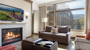 A modern living room with a fireplace, a large window with a mountain view, a flat-screen TV, and a cozy seating area.