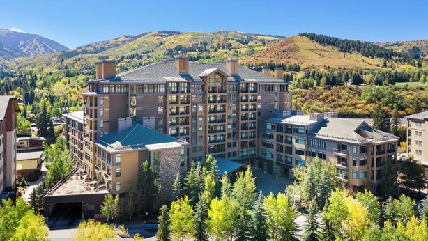 A multi-story hotel with a central courtyard, surrounded by lush greenery and mountains in the background.