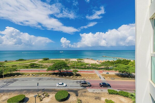 Una carretera costera con vehículos, una playa y un cielo azul despejado.