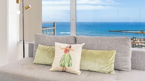 A grey sofa with two cushions, one with a dancer illustration, and a view of the ocean through large windows.
