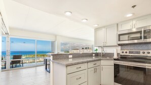 A modern kitchen with a large island, stainless steel appliances, and a view of the ocean.