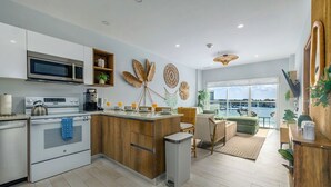 A modern kitchen with a central island, built-in oven, microwave, and coffee maker. There is a dining area with a view of the water. - Beach Vibes Ocean View Condo (Oranjestad)