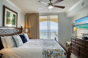 A hotel room with a bed, a ceiling fan, a TV screen, and a view of the ocean.