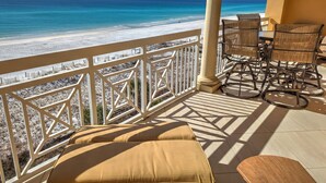 Un balcón con vista a la playa, muebles de exterior y una barandilla blanca.