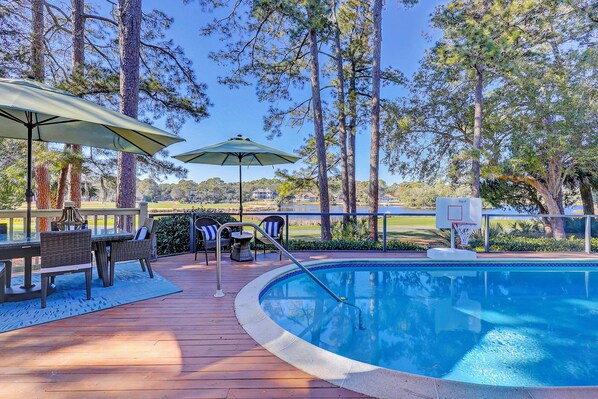 A pool area with a wooden deck, outdoor seating, and a basketball hoop.