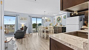Una cocina moderna con encimera de mármol, comedor con sillas blancas y balcón con vistas.