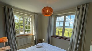 A bedroom with a large bed, two windows, a radiator, and a hanging light fixture. - Charming cottage, sea and garden, close to the D-Day landing beaches, sleeps 6 (Quinéville)