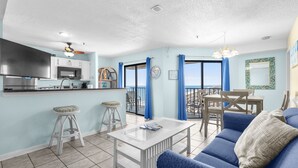 Una cocina moderna con televisor de pantalla plana, un comedor con mesa y sillas, una sala de estar con sofá, y un balcón con vistas.