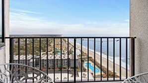 En balkon med udsigt over en strand, en swimmingpool og en parkeringsplads.