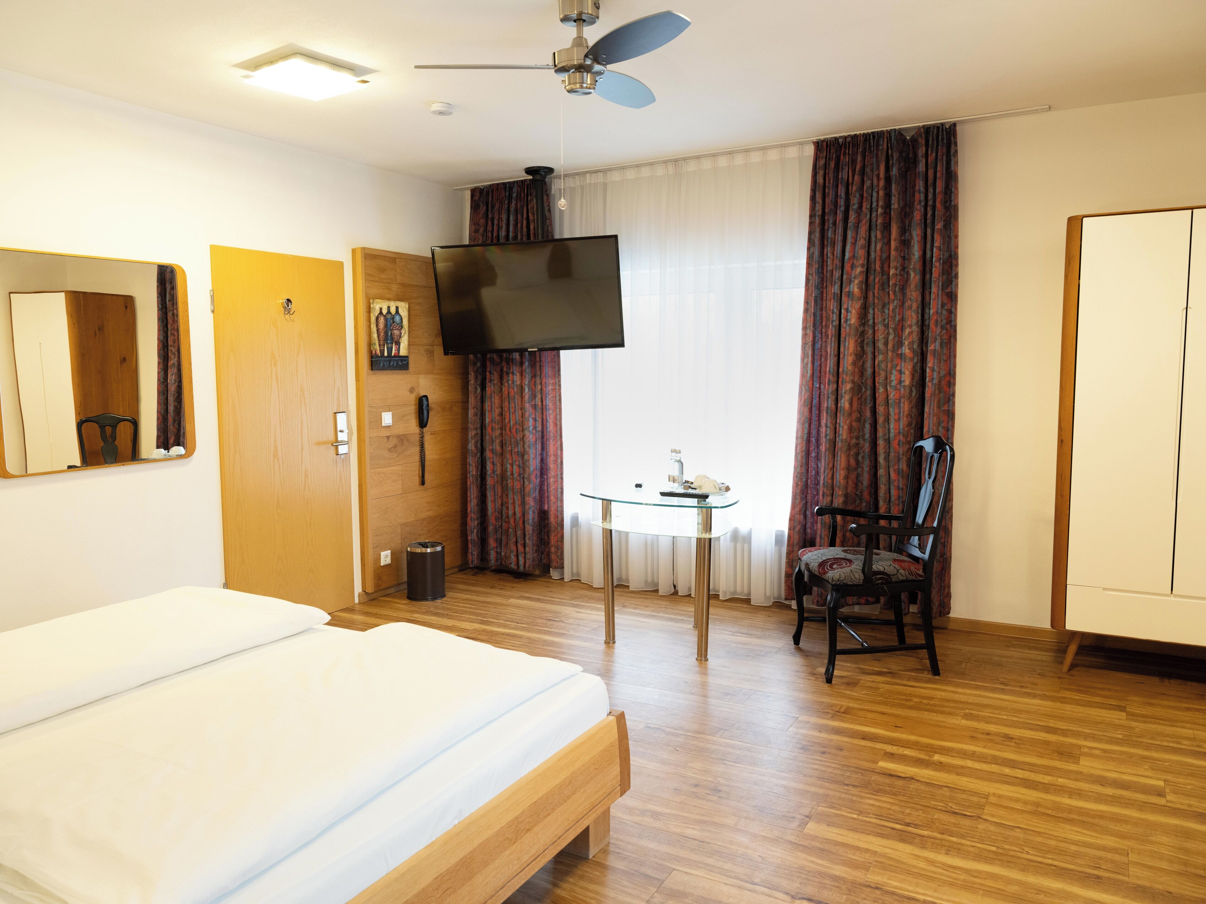 Habitació d'hotel amb llit, televisió, cadira, taula petita i armari.