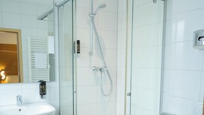 Moderni kylpyhuone, jossa on lasiseinällä varustettu suihku, valkoinen pesuallas ja wc.