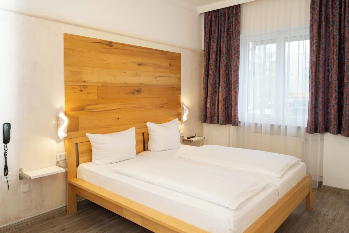 A double bed with a wooden headboard, white bedding, and a bedside table with a lamp.