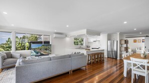 A modern living room with a grey sofa, wooden flooring, and a large window overlooking a scenic view.
