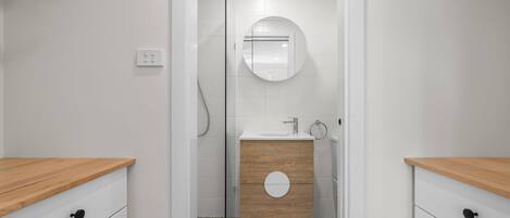 A modern bathroom with a wooden vanity, a round mirror, and a shower area.
