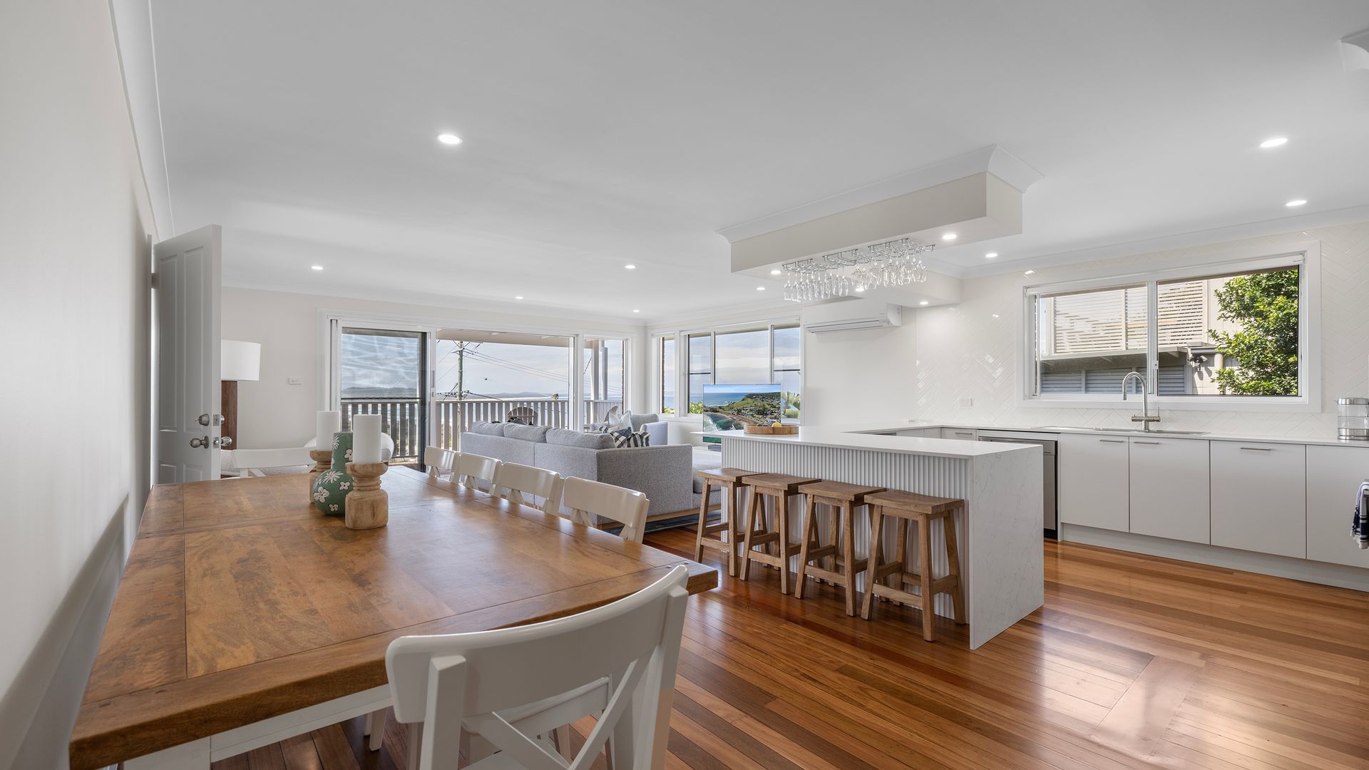 A modern kitchen with a central island, a dining area with a wooden table, and a balcony with a view.