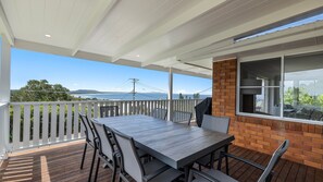 A covered outdoor patio with a wooden table and chairs, a brick wall, and a view of the ocean.