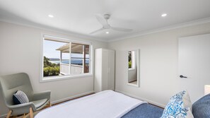 A bedroom with a bed, a chair, a wardrobe, and a window with a view of the sea.