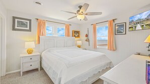 A bedroom with a bed, a nightstand, a lamp, a ceiling fan, and a window with curtains. - Soundfront Home in Frisco with Hot Tub, Private Dock and Windsurfing Access (Frisco)
