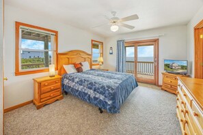 A bedroom with a bed, a nightstand, a dresser, a ceiling fan, a window with a view, and a door leading to a balcony. - Soundfront Home w/ Private Windsports Access, Hot Tub, Stunning Views (Waves)