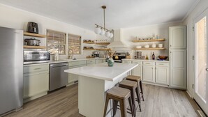 A modern kitchen with white cabinetry, a central island with stools, and a variety of appliances including a refrigerator, microwave, and oven. - Splash House - Heated Pool, Hot Tub, Pickleball, Movie Theater (Asheville)