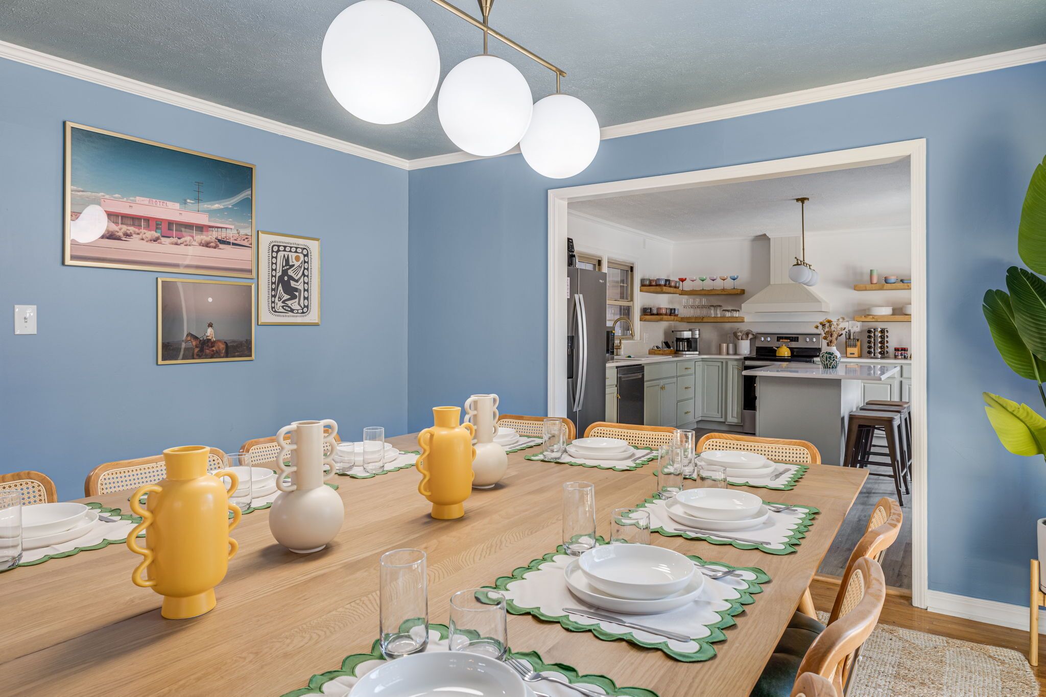 Ein Esszimmer mit einem langen Tisch, gedeckt für eine Mahlzeit, einer Küche im Hintergrund und Wandbildern.