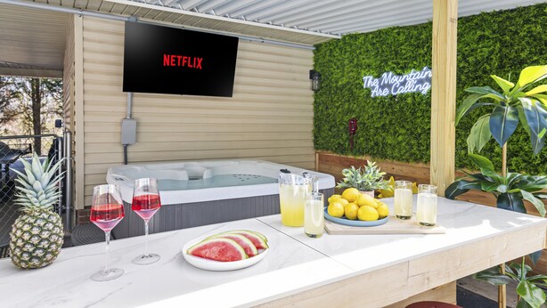 A bar area with a Netflix screen, a hot tub, and a wall with a sign that says "The Mountain Calling". - Splash House - Heated Pool, Hot Tub, Pickleball, Movie Theater (Asheville)