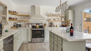 A modern kitchen with white cabinets, stainless steel appliances, and wooden shelves. - Splash House - Heated Pool, Hot Tub, Pickleball, Movie Theater (Asheville)
