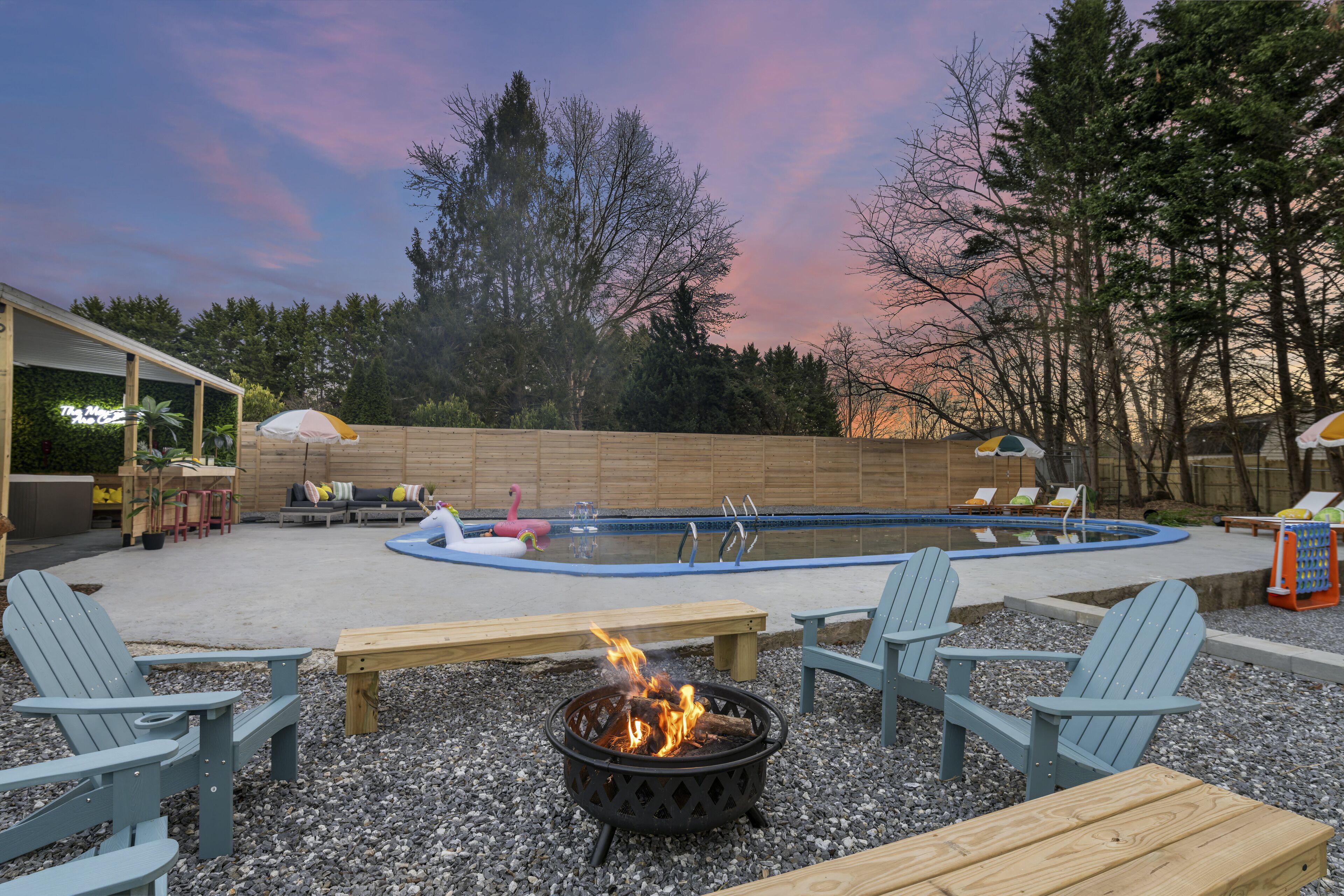 Un área de piscina al aire libre con sillas Adirondack, un hogar para fogata y sillones de descanso.