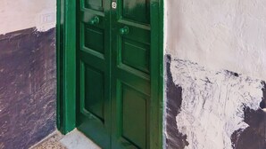 Eine grüne Tür mit rotem Notlicht, eine weiße Wand mit abblätternder Farbe und ein Terrazoboden.