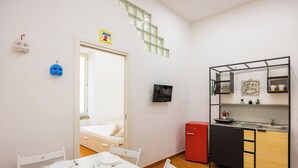 Ein kleiner Raum mit einem Bett, einem Esstisch mit Stühlen, einer Kochnische und einem Fernseher.