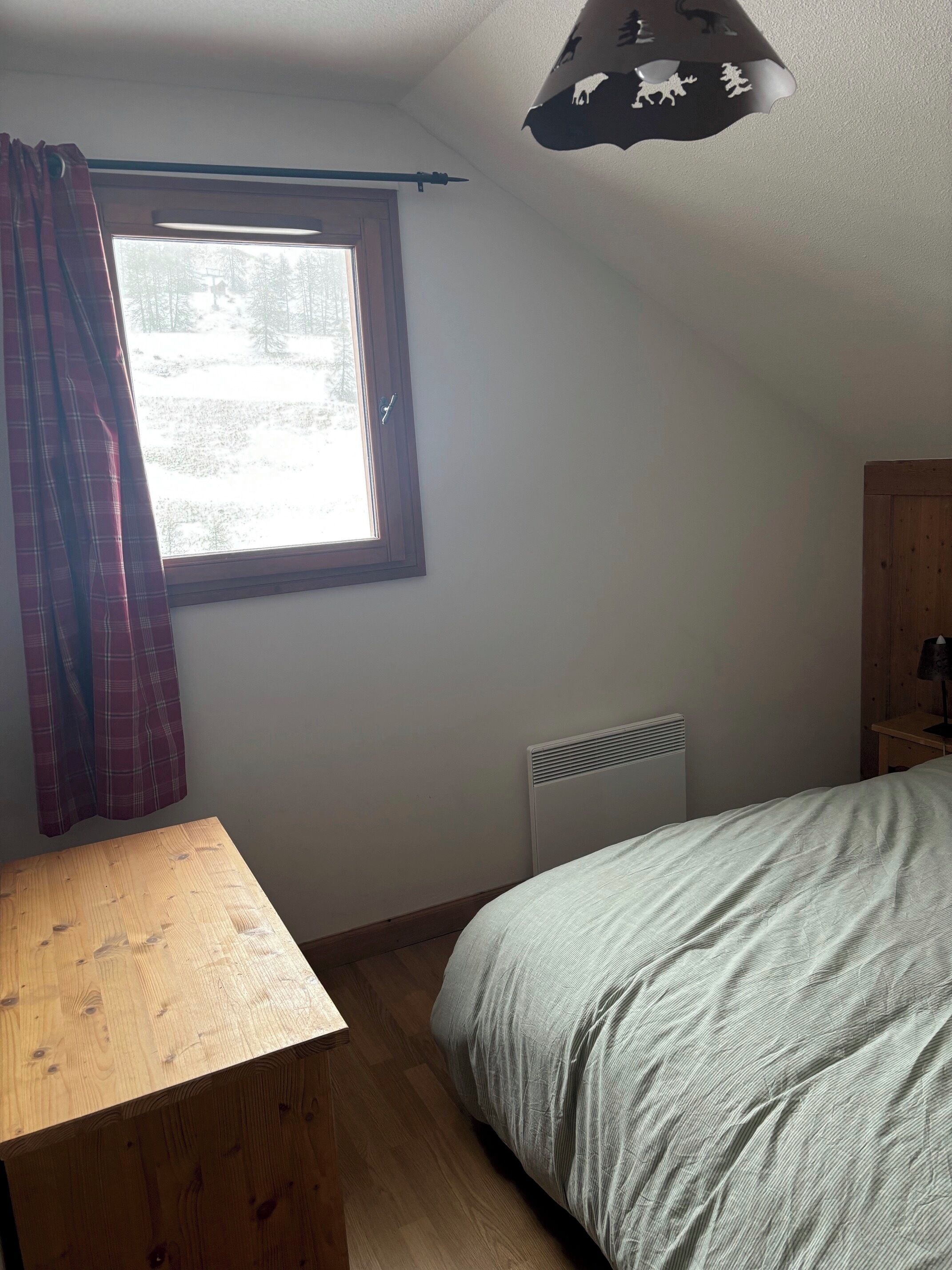 Een slaapkamer met een bed, een houten tafel, een radiator en een raam met gordijnen.