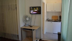 Une cuisine compacte avec une petite table à manger, un ventilateur et un téléviseur fixé au mur.