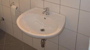 Une salle de bain avec un lavabo blanc, un miroir au-dessus et des toilettes sur la gauche.