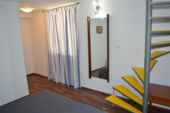 A room with a wooden floor, a striped curtain, a mirror, and a yellow staircase.