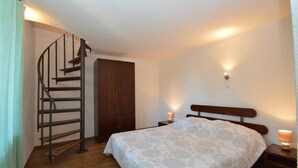 Een slaapkamer met een bed, een houten garderobe, een spiltrap en een nachtkastje met een lamp.