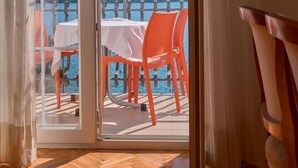Une pièce dotée d’un plancher en bois, d’une porte-fenêtre coulissante donnant sur un espace extérieur avec des chaises et une table orange, et offrant une vue sur une étendue d’eau et une végétation luxuriante.