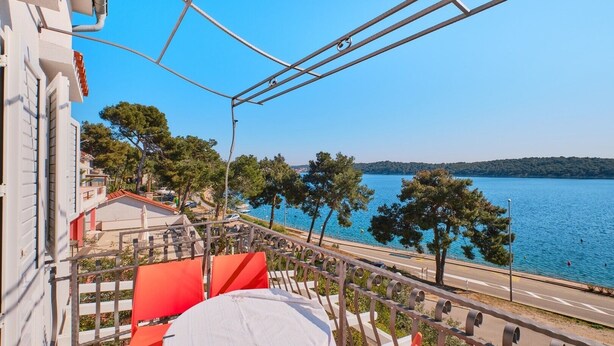 Un balcon donnant sur un lac, avec des chaises rouges et un parasol blanc.