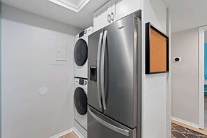 A compact kitchen with a stainless steel refrigerator, a built-in washing machine, and a small wooden door.