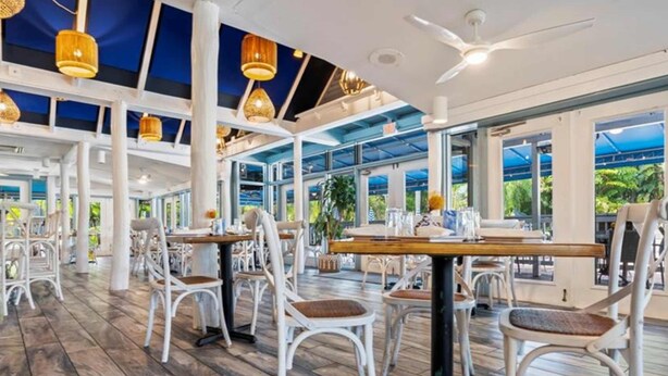 An indoor dining area with white chairs, tables, and a high ceiling with exposed beams.