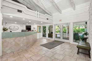 A reception area with a counter, a sign reading 'Park Shore Resort,' and a view of the outdoors through glass doors. - H-248 - Luxury Corner Unit - Updated with Views (Naples)