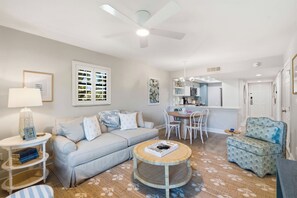 A modern living room with a sofa, a coffee table, a dining area with chairs, a kitchen with a microwave, and a ceiling fan. - H-248 - Luxury Corner Unit - Updated with Views (Naples)