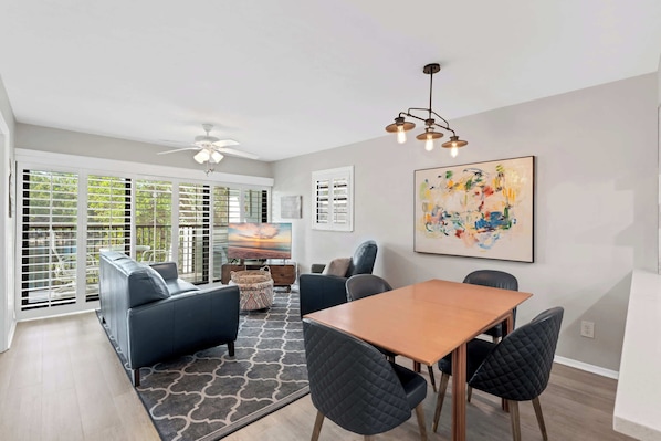 A modern living room with a sofa, chairs, a dining table, and a ceiling fan.