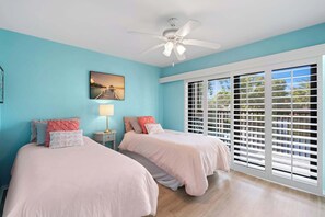 A bedroom with two beds, a ceiling fan, a window with blinds, and a painting on the wall.